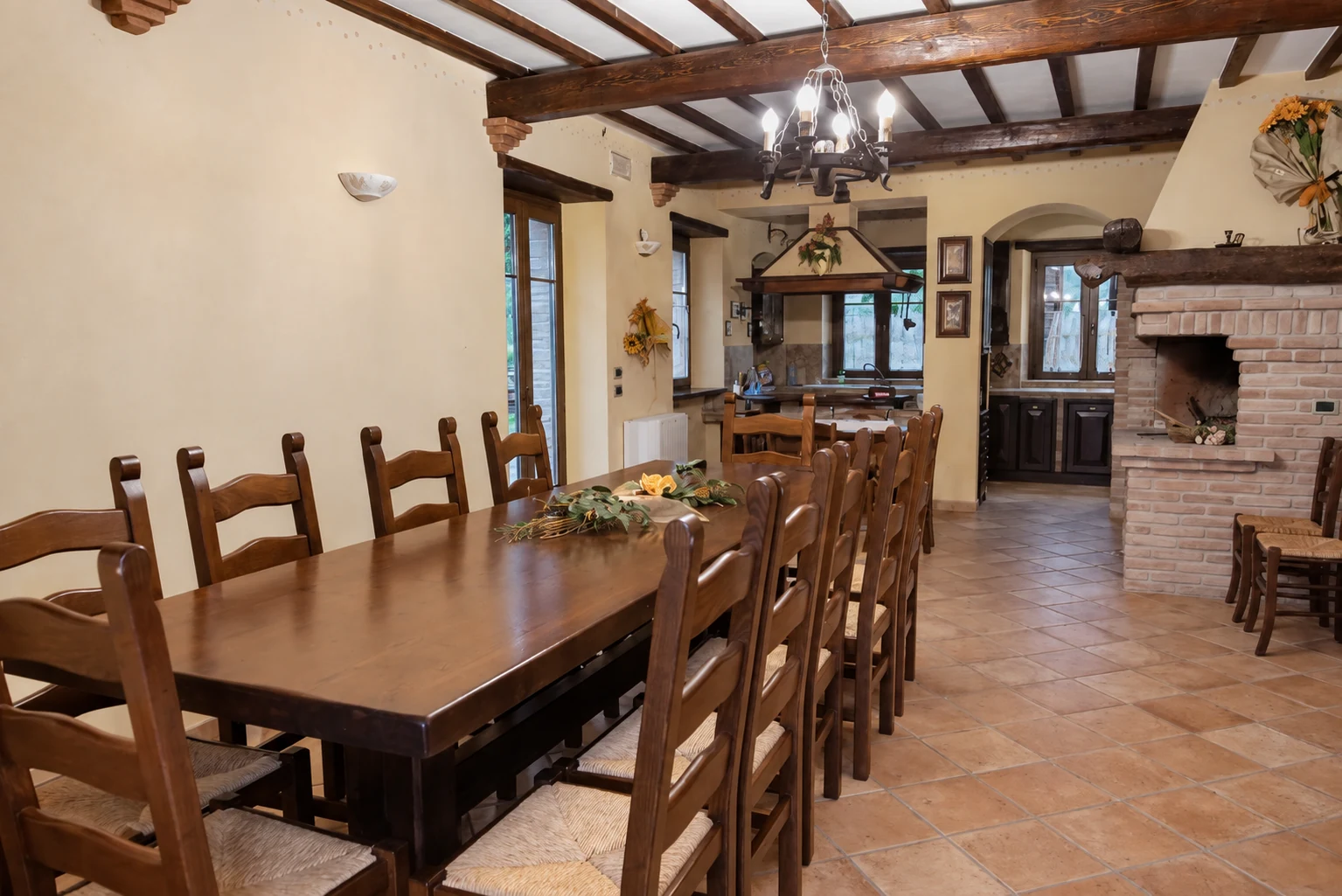 Il lungo tavolo del soggiorno, con il camino e la cucina sul fondo